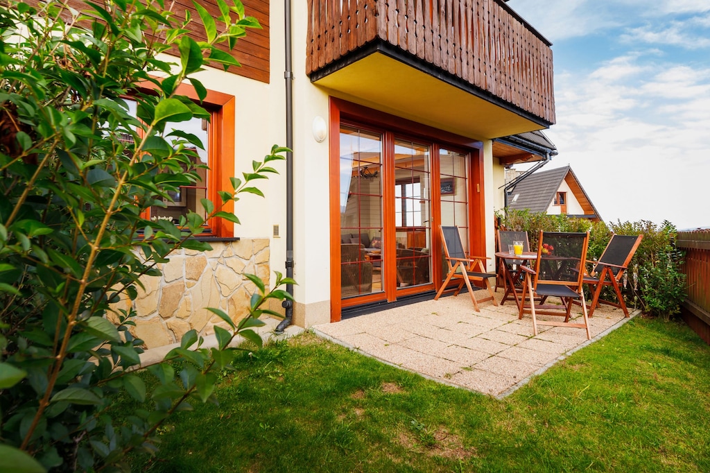 A small patio with grass and shrubs, along with a wooden fence and a partial view of the building.