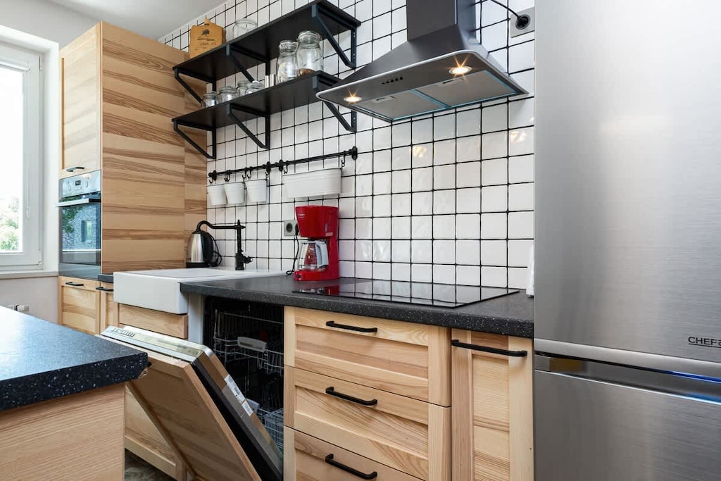 A sleek and modern kitchen featuring wooden cabinets, stainless steel appliances, and an open shelving design with a tiled backsplash.