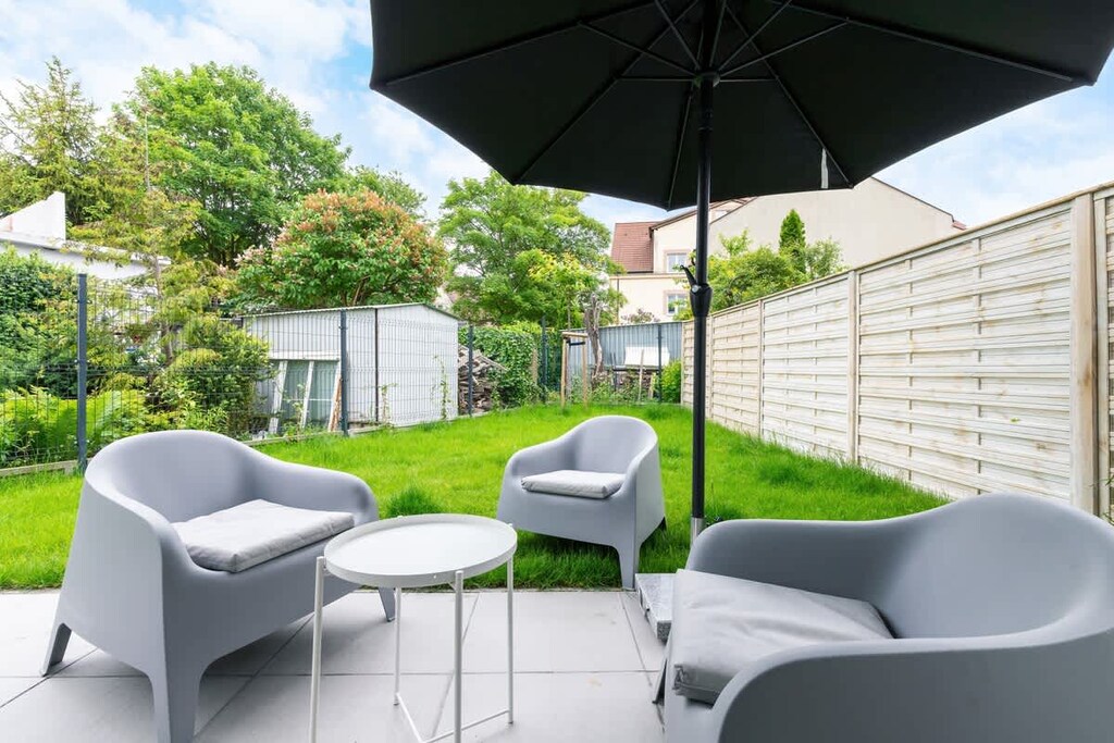 Outdoor seating area with gray furniture and umbrella, next to a small lawn.