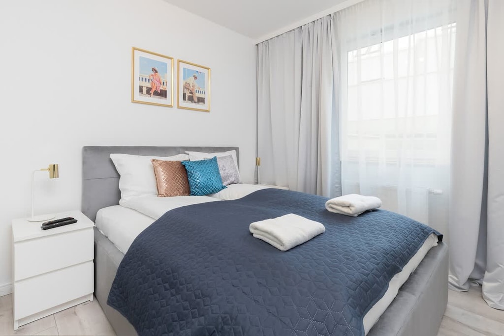 Bedroom with blue bedspread, white walls, and large window.