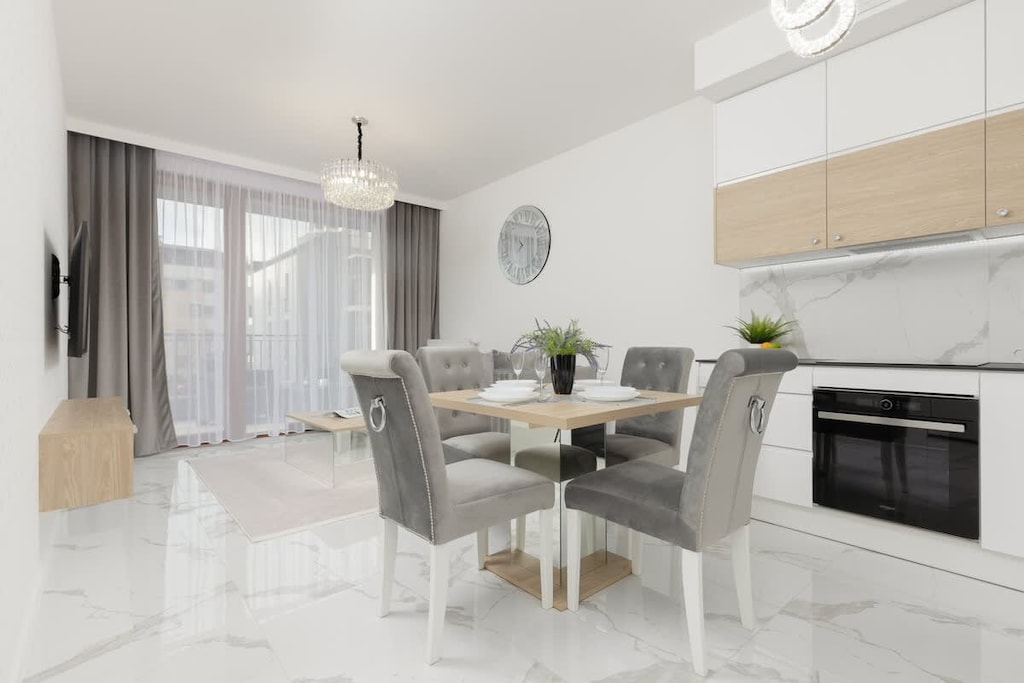 An open-plan kitchen and dining area with light wood cabinets, modern appliances, and a glass dining table with grey chairs.
