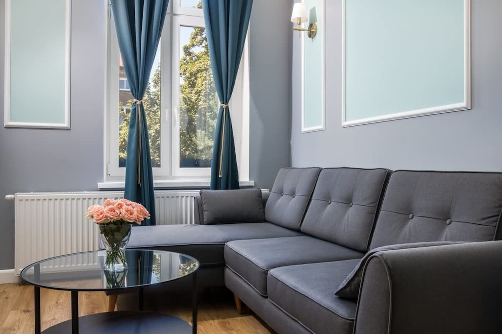A stylish living area with a dark gray sofa, a round coffee table, and large windows framed by deep blue curtains, creating an elegant atmosphere.

