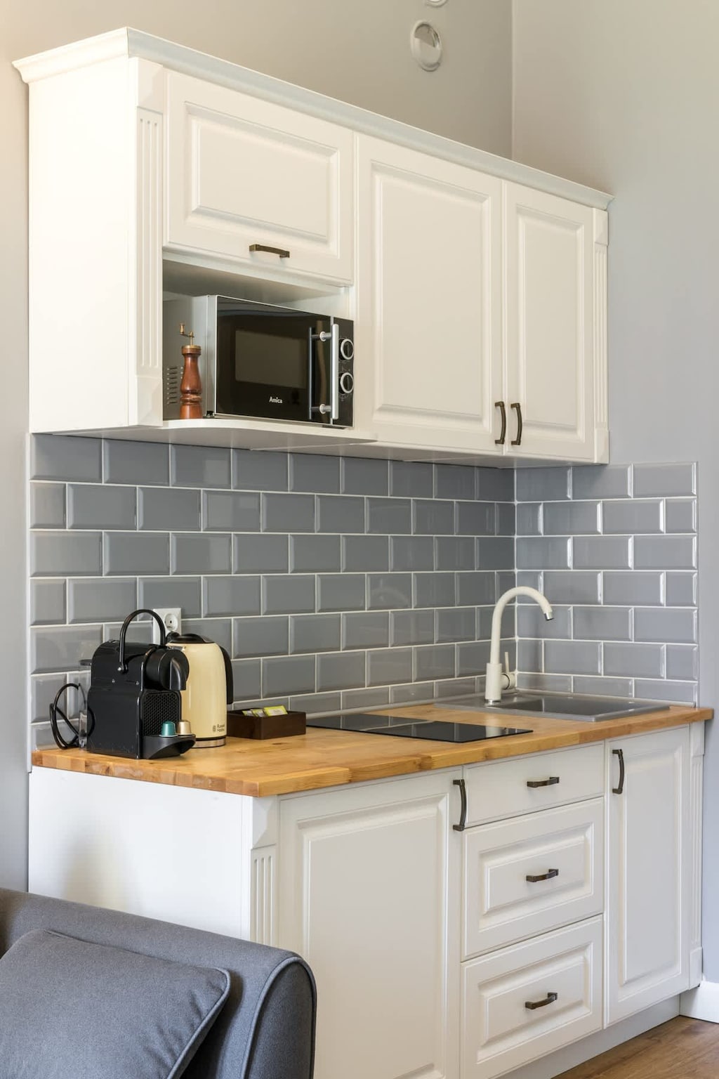 A compact kitchenette with white cabinets, a gray subway-tile backsplash, and essential appliances for convenience.

