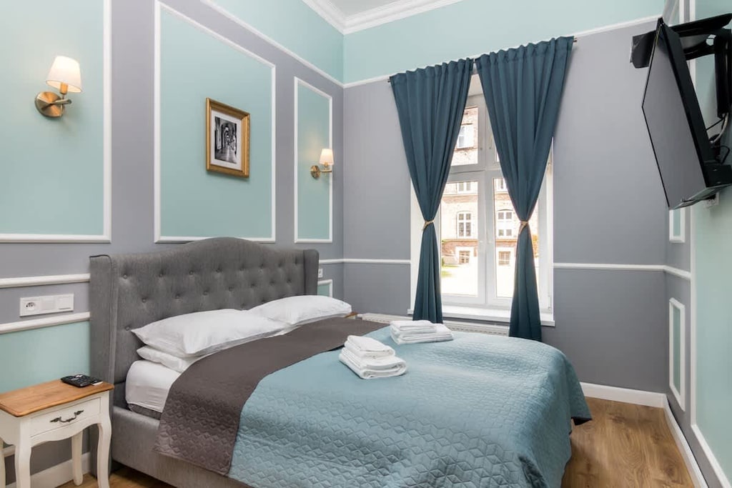 Another angle of the bedroom, highlighting deep blue curtains, classic wall molding, and a soft, inviting bed.

