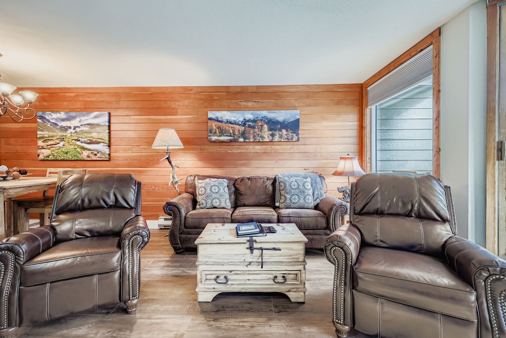 Relax in your spacious living room with comfortable leather seating, warm wood paneling, and mountain artwork creating the perfect atmosphere for unwinding after your adventures.