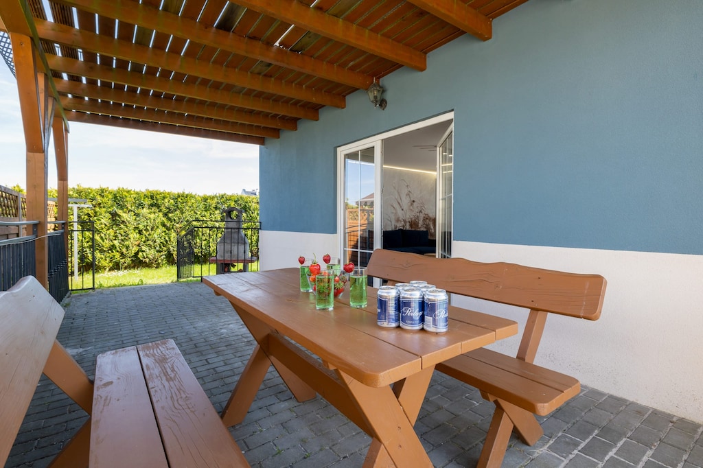 A charming wooden patio set, complete with benches and a table laid for a meal, situated under a sheltered area with warm lighting, perfect for enjoying outdoor gatherings.