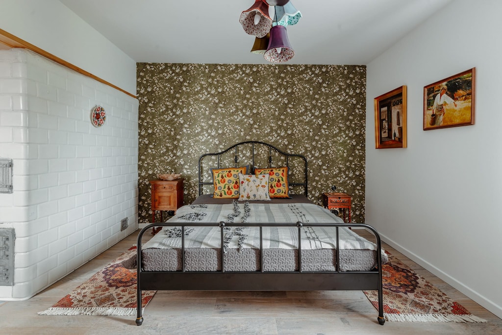 A charming bedroom with an antique metal bed frame, patterned wallpaper, and elegant wooden furniture.