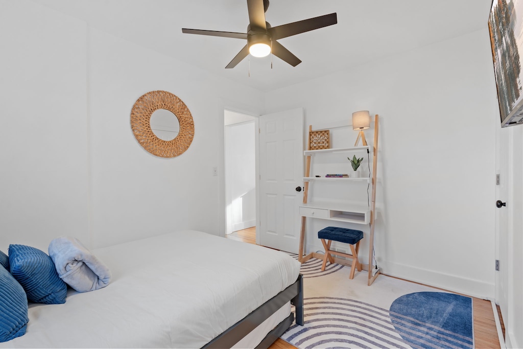 Relax in your bright, airy bedroom with coastal blue accents, modern workspace, and gentle ceiling fan keeping you cool.