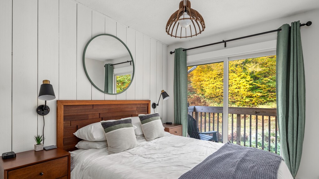 - Bedroom with queen bed balcony access and forest views - Bright decor with mirror and soft linens creates comfort - Peaceful retreat for restful nights during Vermont stays