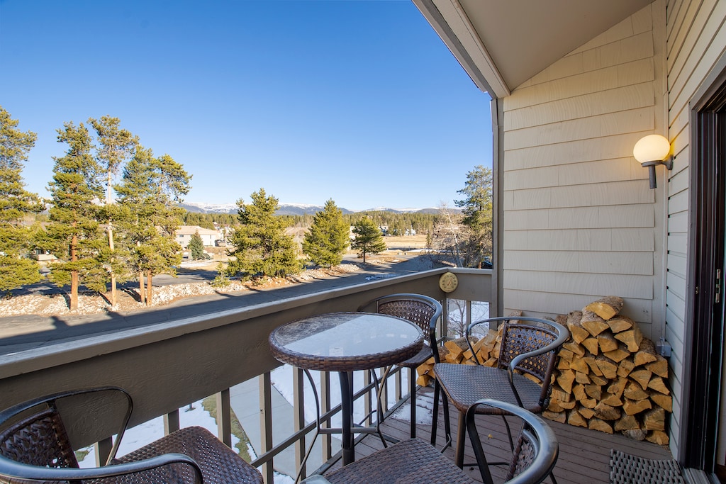 A small balcony with a bistro dining set, and a stack of firewood ready for a warming fire