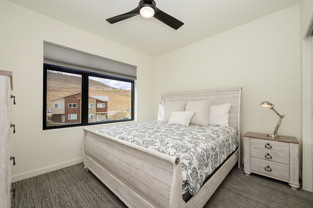 - Bright bedroom with large window framing hillside and community views   - Plush bedding and sleek ceiling fan add comfort for restful nights   - Modern furnishings and natural light create a peaceful mountain escape