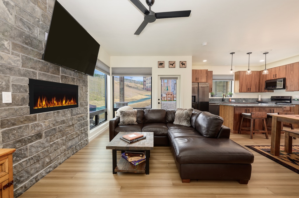- Cozy living room with leather sectional and stone fireplace ambiance   - Wall-mounted TV and warm fire create the perfect spot for movie nights   - Open layout connects living space seamlessly to the modern kitchen