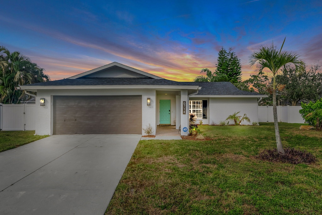 Single-story house with a two-car garage, a light blue front door, and a manicured lawn, set against a vibrant sunset sky.