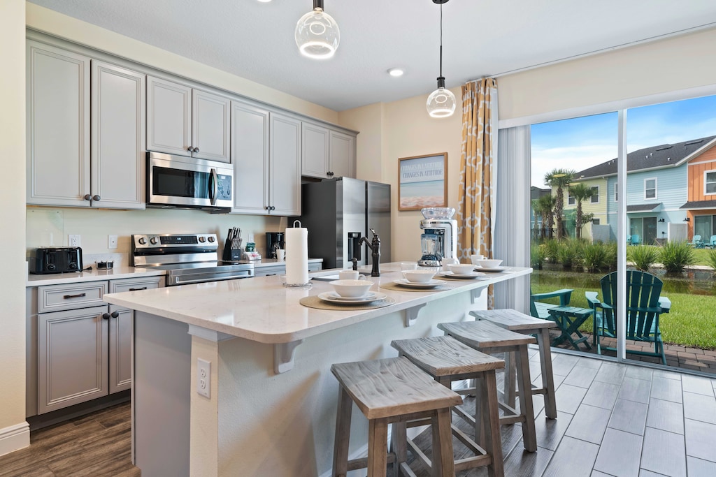 Modern, fully equipped kitchen featuring stainless steel appliances and cabinetry - Large island with a white marble countertop, seating for four, and stylish pendant lighting - Sliding glass door provides plenty of natural light with a scenic view