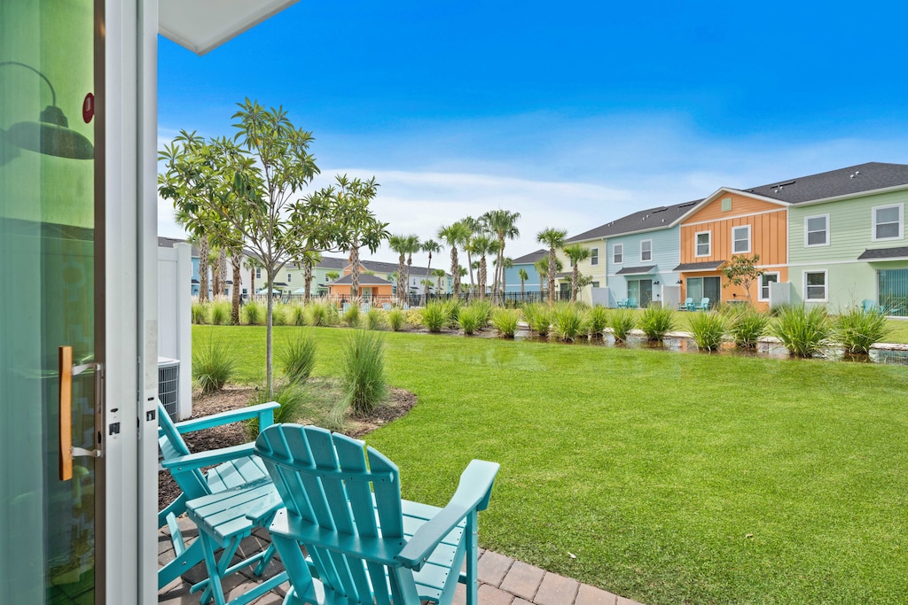 Cozy patio with turquoise Adirondack chairs, ideal for morning coffee or evening relaxation - Lush green lawn and scenic area with palm trees and ornamental grasses, creating a tranquil retreat - Colorful townhouses, adding vibrant charm