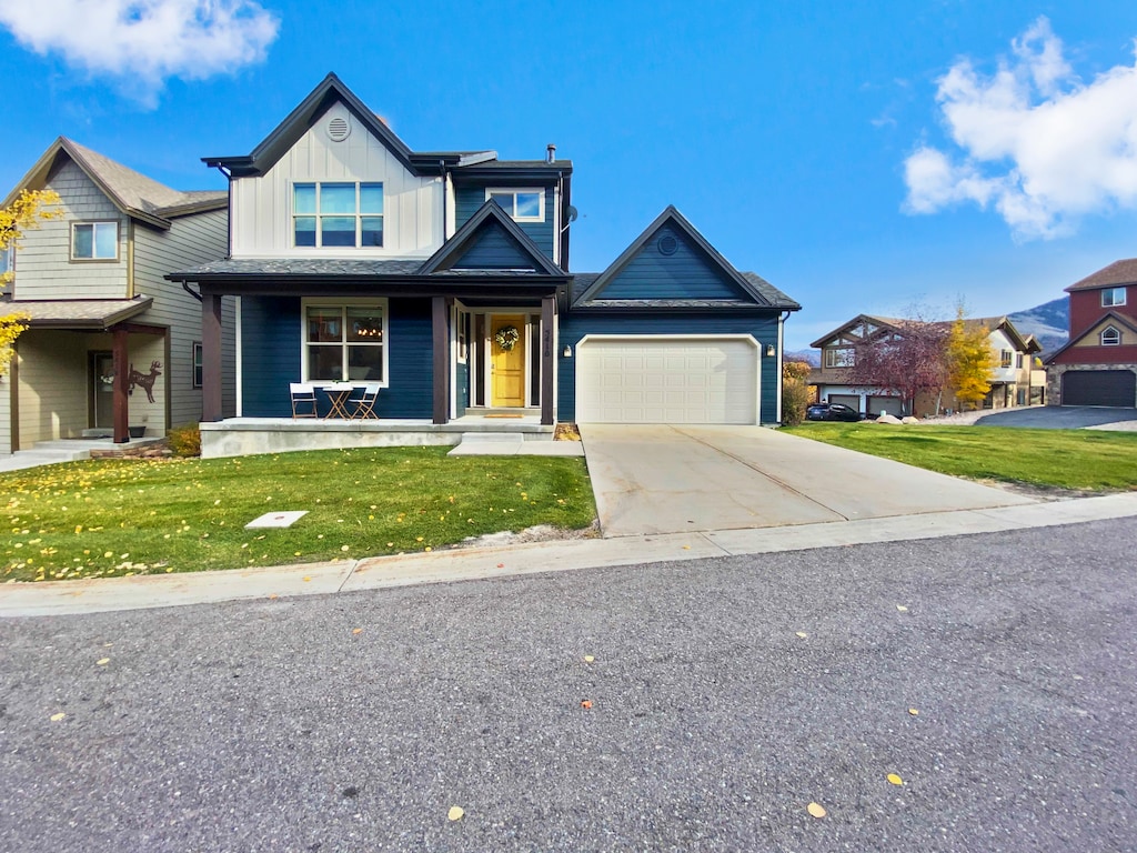 A two-story house with a beige garage and blue siding, featuring a front porch and a small table with chairs. Located on a suburban street with similar houses and a mountain visible in the background.