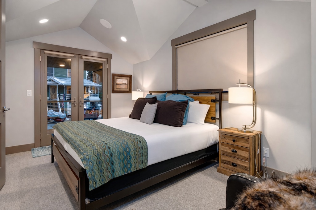Unwind in your elegantly appointed bedroom featuring plush bedding, warm wood accents, and French doors opening to mountain views.