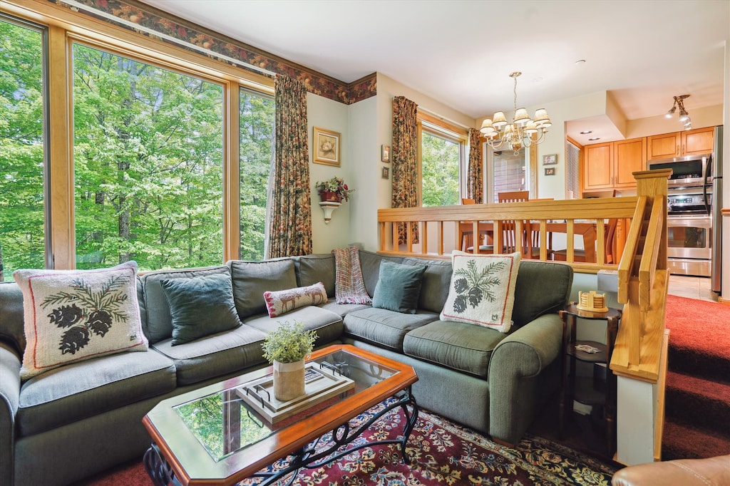 Inviting living room filled with natural light and surrounded by forest views. Features a spacious sectional and open layout connecting to the dining and kitchen areas.