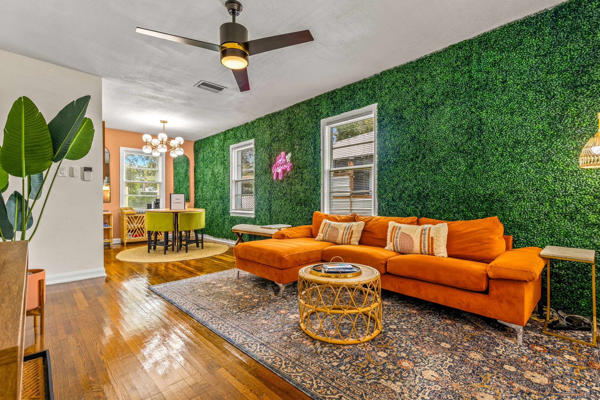 Feel the warmth and charm of our living room with its orange plush sofa, stylish grass wall design, and neon ‘hello gorgeous’ light for a touch of flair