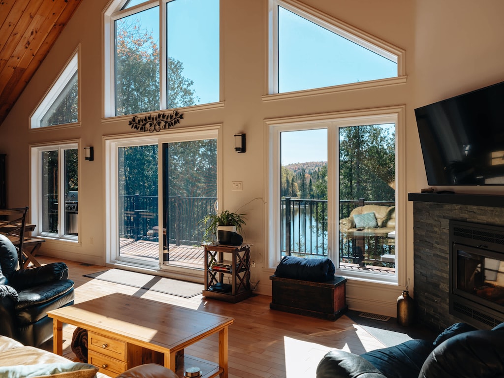 Floor-to-ceiling windows frame Lake Lise with comfortable seating TV and fireplace