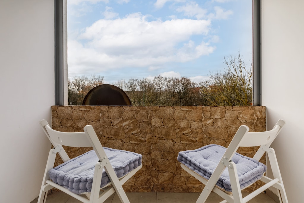 A small balcony with a wooden table, chairs, and a lovely outdoor view.
