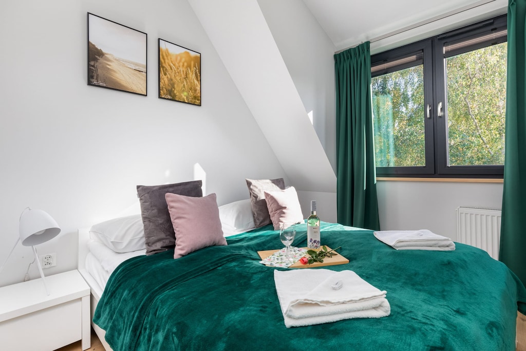 A comfortable bedroom with a double bed, green bedding, pink throw pillows, and a view of the slanted ceiling.