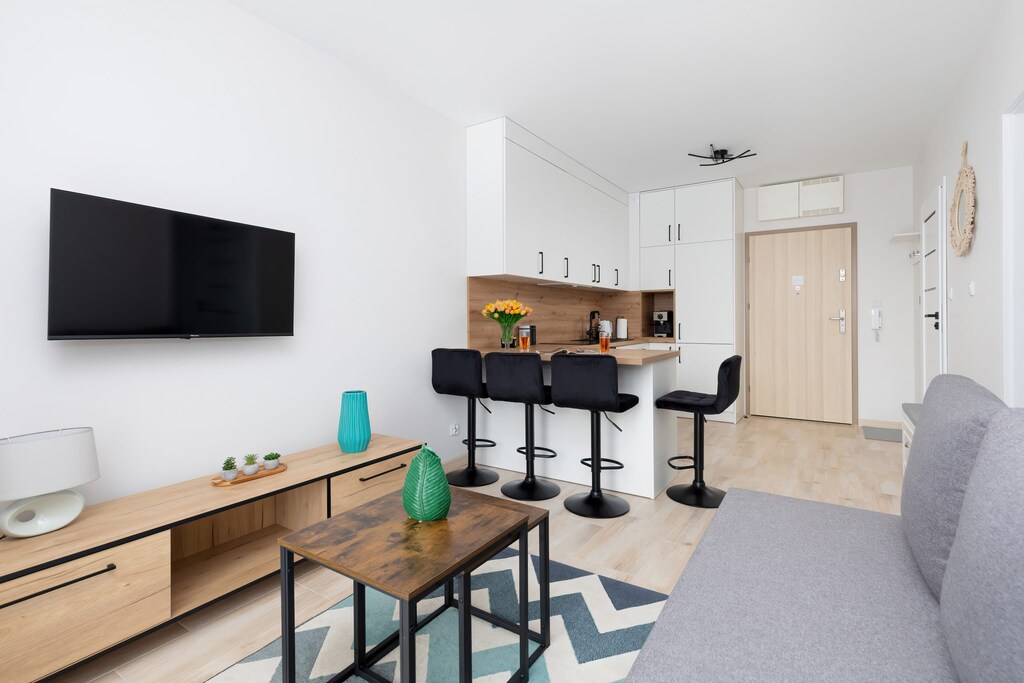A modern living room with a sofa, coffee table, wall-mounted TV, and light decor.

