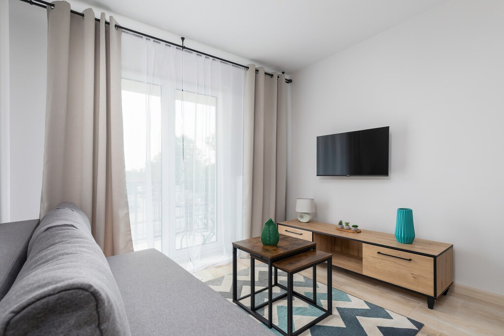 Another perspective of the living room, showing a stylish TV stand and large windows.

