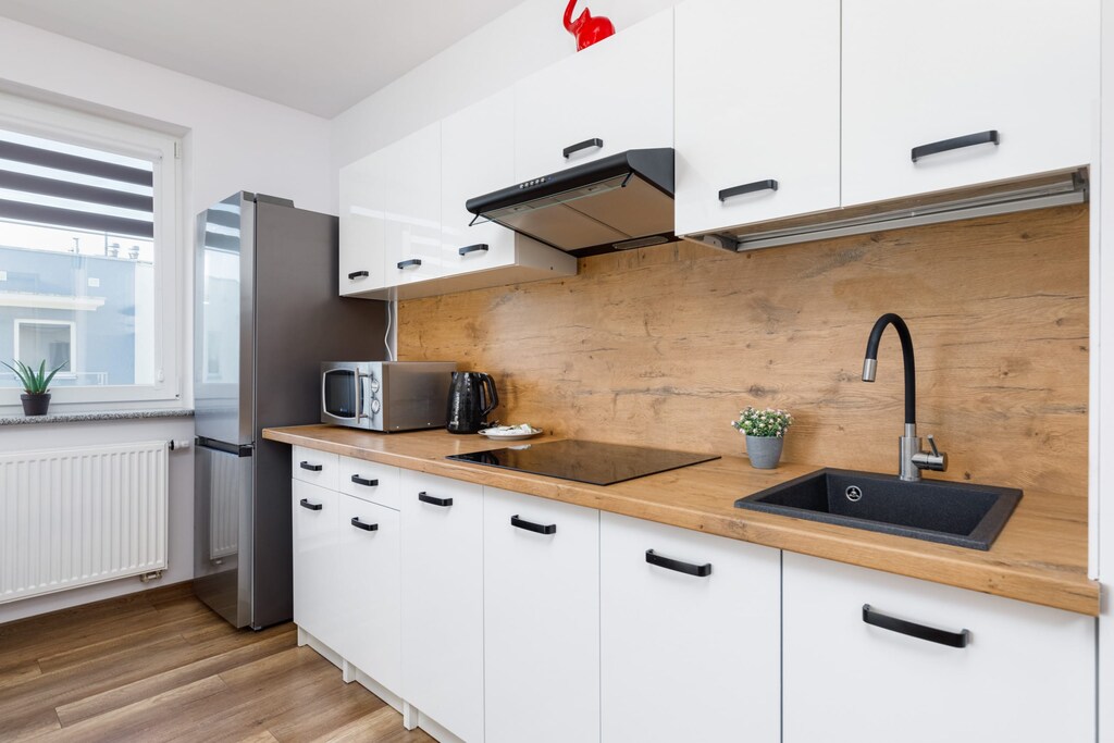 A sleek and modern kitchen with white cabinets, wooden countertops, and black fixtures. The space is fully equipped with appliances for cooking.