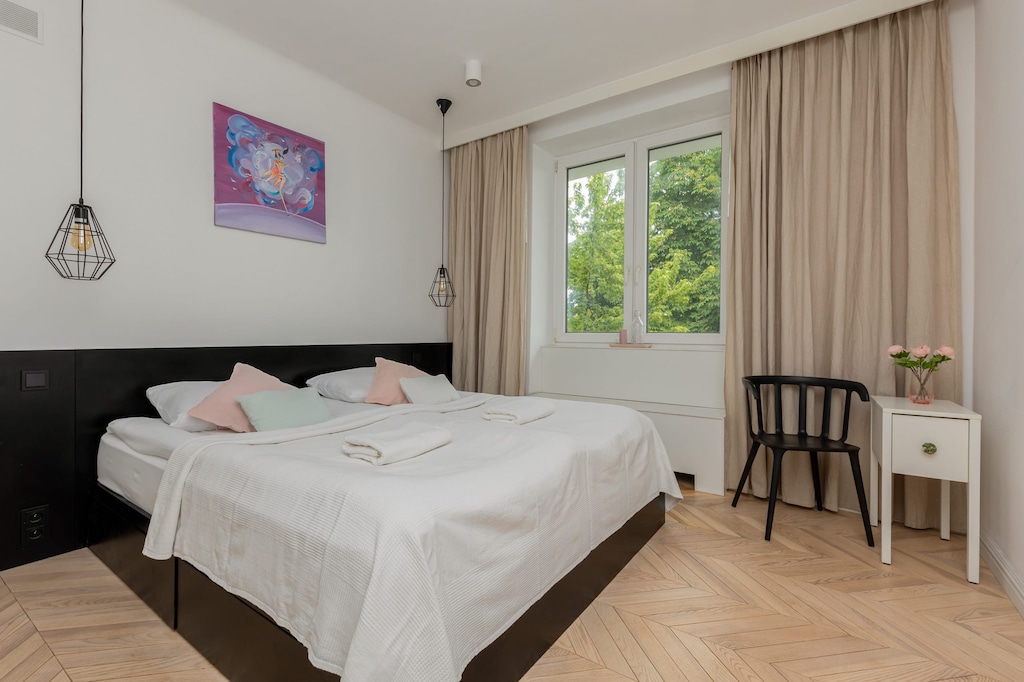 A cozy bedroom featuring a double bed, colorful wall art, and a window overlooking greenery.
