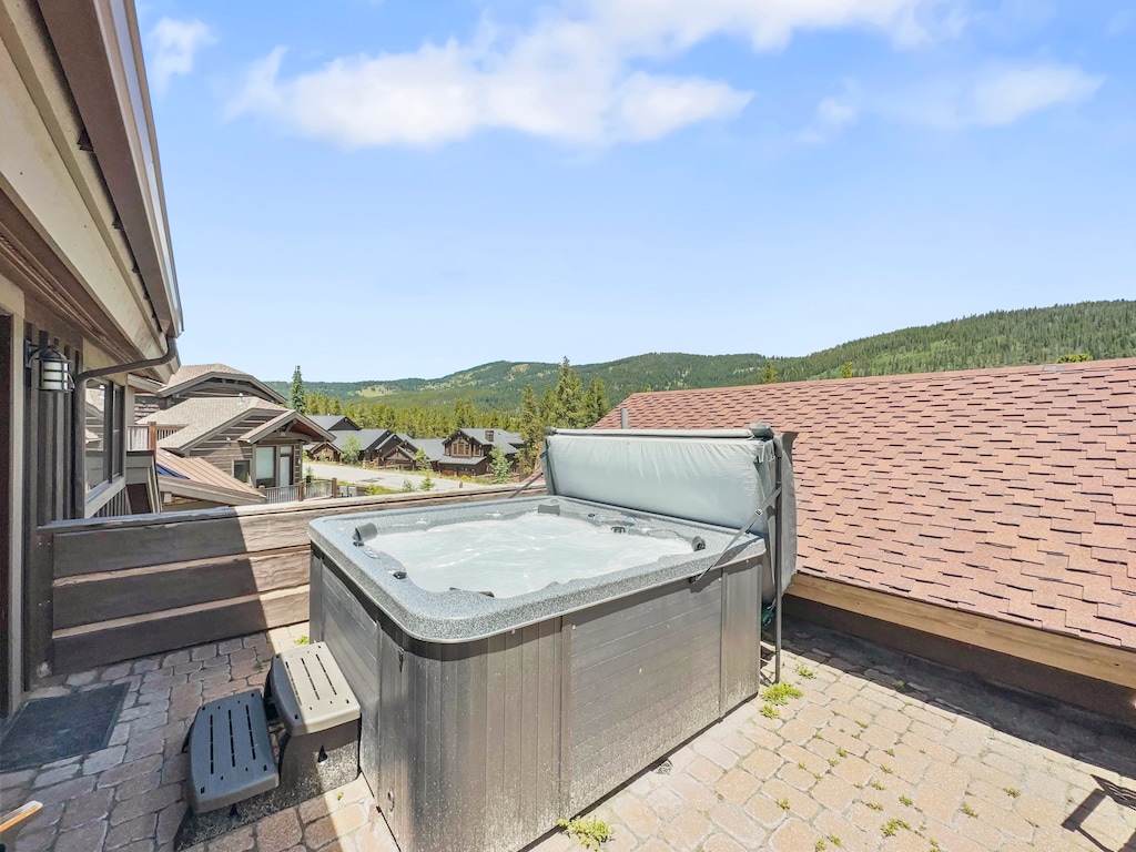 Outdoor hot tub on a stone patio with a view of houses and mountains in the background.