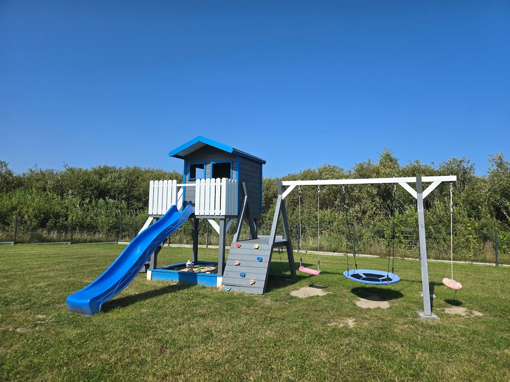 Outdoor playground featuring a slide and swing set surrounded by an open grassy area.

