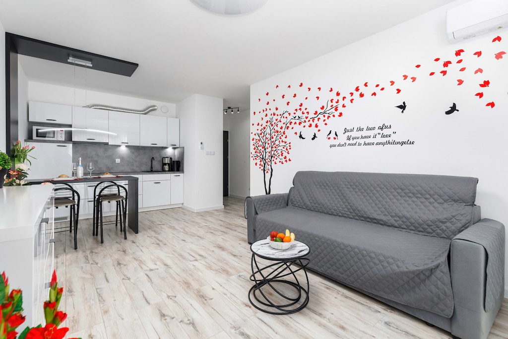 Spacious living room with a modern sofa, decorative wall accents, and a bright dining area, ideal for relaxation.
