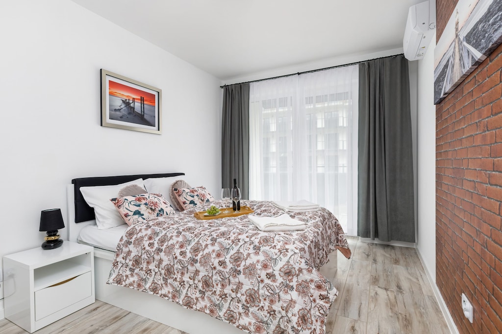 Cozy bedroom with a comfortable double bed, stylish bedding, and access to natural light through large windows.
