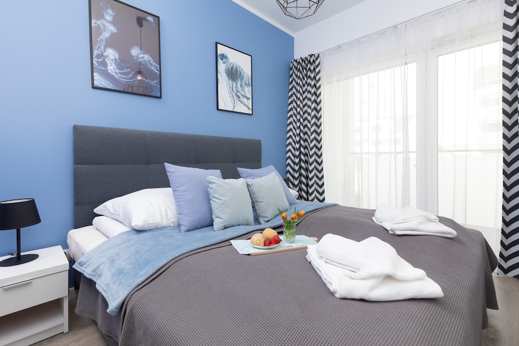 A spacious bedroom with a large bed dressed in blue and white linens. The walls feature artwork that adds character to the space.