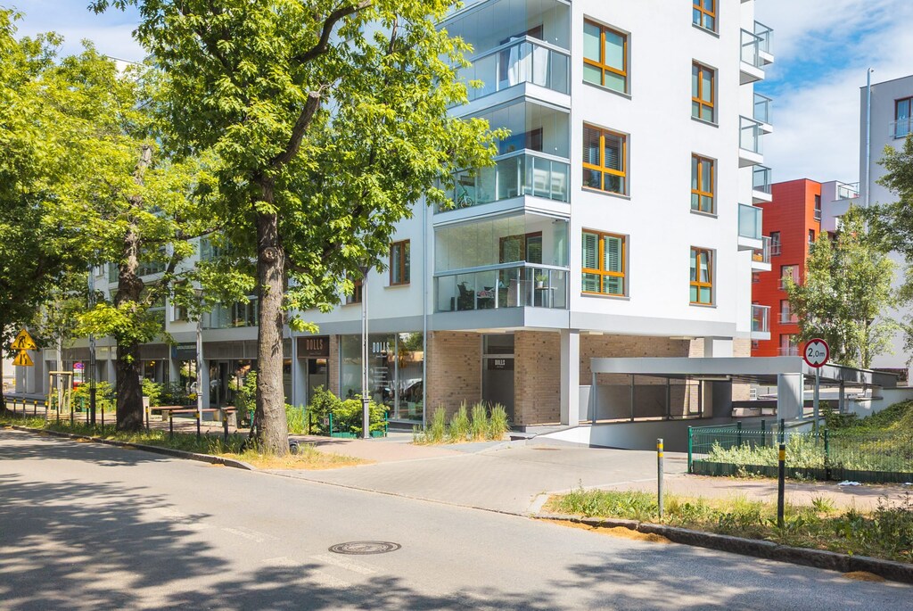 A modern apartment exterior with well-maintained sidewalks and surrounding greenery. Tall, stylish residential buildings are in the background.