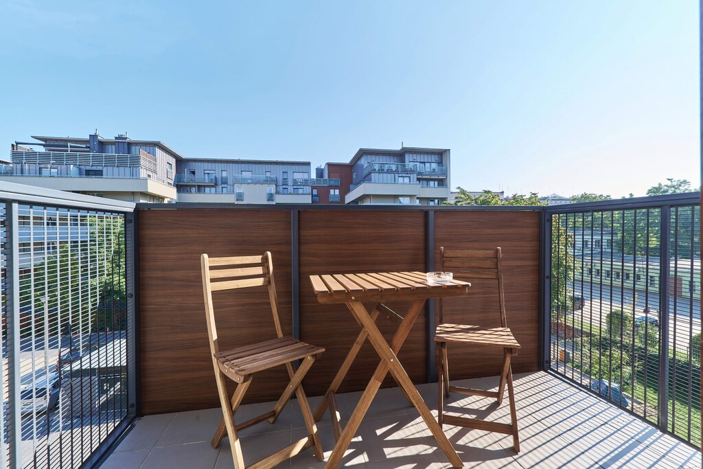 A comfortable seating area on a balcony with wooden chairs and a table, surrounded by a lush, peaceful outdoor view.