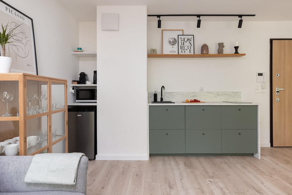 A modern kitchen with a simple design, featuring light green cabinetry and open shelving, giving it a clean and uncluttered appearance.