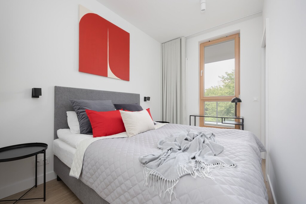 A cozy bedroom with red and white decorative accents and a bed placed near a sliding glass door.
