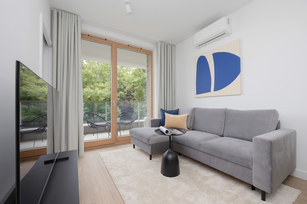 A modern living room with a gray sofa, abstract wall art, and floor-to-ceiling windows offering a view of the balcony.