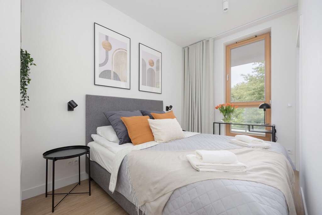 A bedroom with a soft gray bedspread, large framed art, and warm natural light from the window.