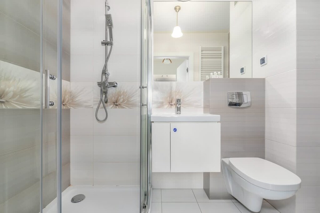 White and grey, modern bathroom with a comfortable shower, a mirror, a welcoming toiletries set, and towels.