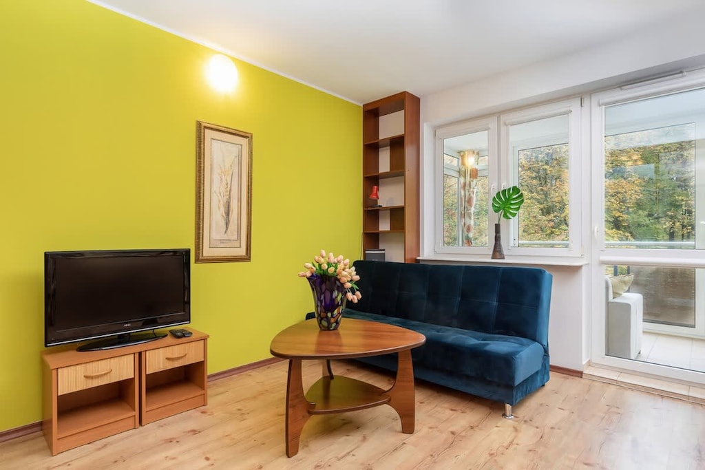  A spacious living room with yellow accent walls, a blue sofa, a wooden coffee table, and a TV stand by the window.
