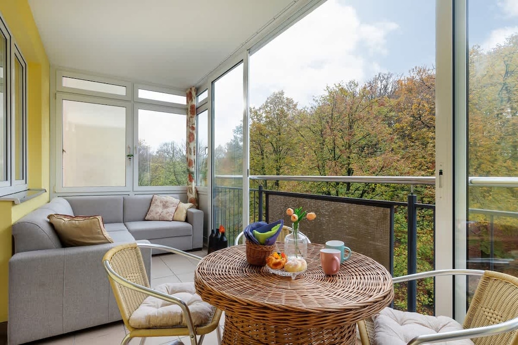 A cozy balcony setup with a small table, chairs, and a view of the surrounding greenery, perfect for relaxation.