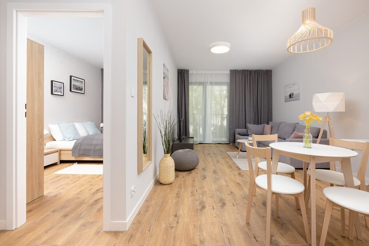 A bright, open-plan living room with a dining area in the background, featuring wooden floors, modern furniture, and soft lighting.