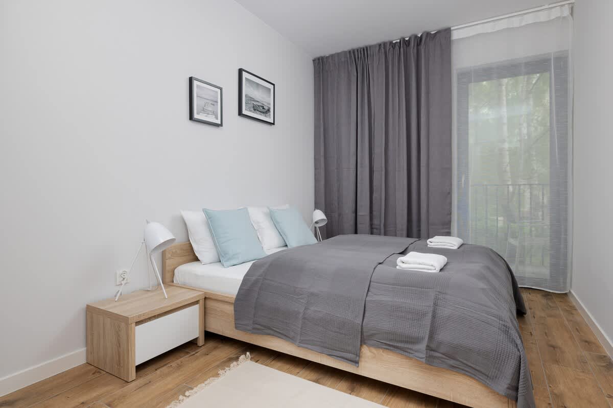 A cozy bedroom with a double bed, pastel-colored pillows, gray bedding, and minimalist decor.