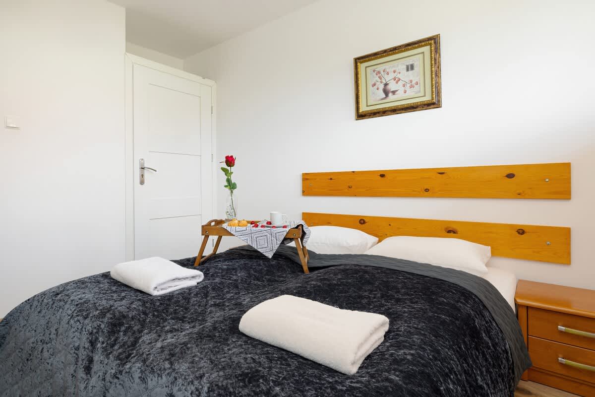 A cozy bedroom with a comfortable double bed, gray bedding, wooden headboard, and bedside table featuring a flower vase.