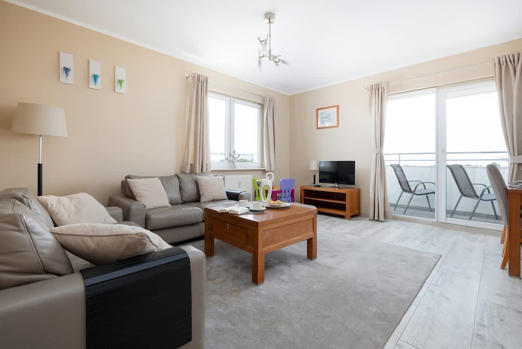 A spacious living room with a beige sectional sofa, wooden coffee table, and light walls, creating a cozy and welcoming atmosphere.