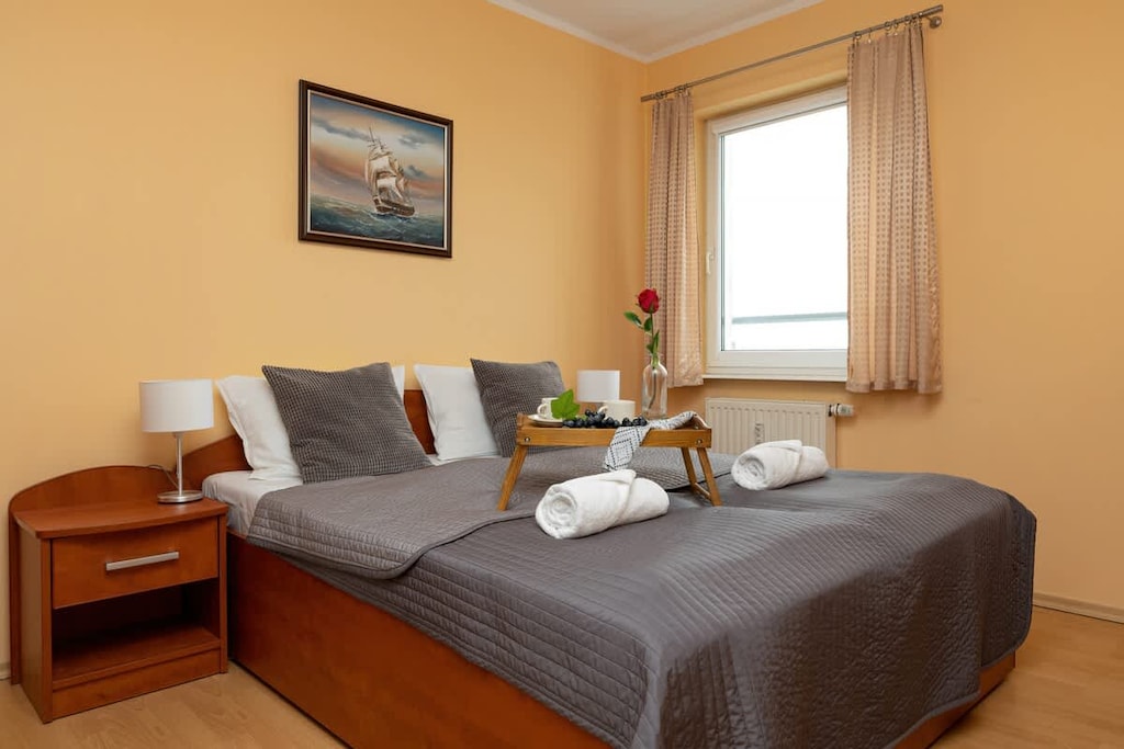 A comfortable bedroom with a double bed, soft gray bedding, and warm yellow walls, featuring a bedside table with a lamp.