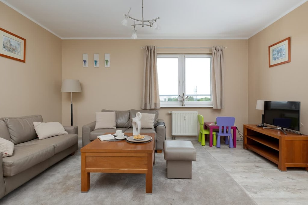 The living room from a different perspective, featuring a large window letting in natural light and a TV on a wooden stand.